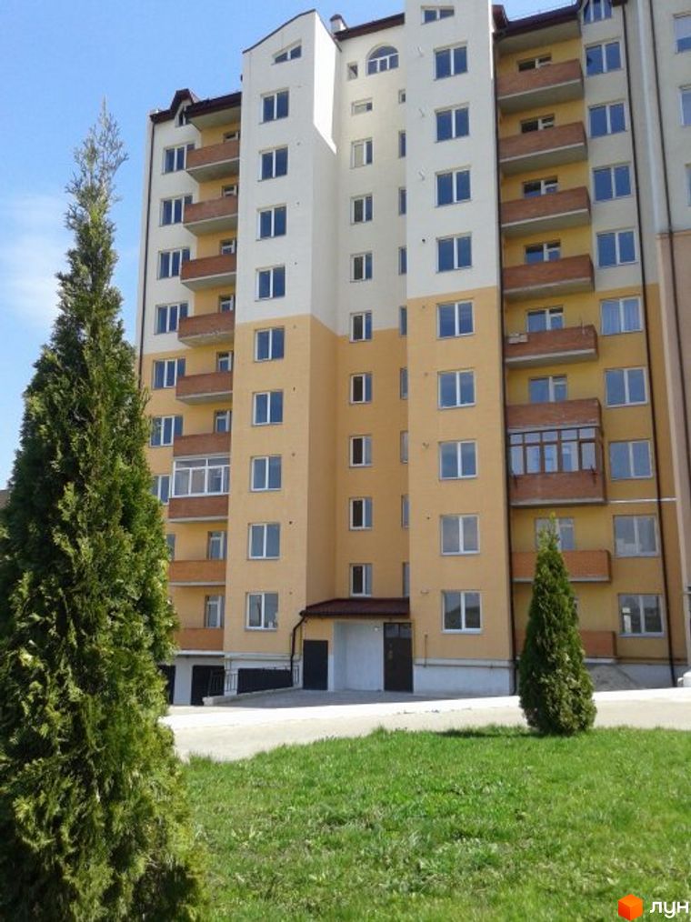 Зовнішній вигляд новобудови на вул. Коновальця, 4а, 4б. Будинок має жовто-білий фасад з балконами та вікнами. Поруч зелена галявина та дерева.